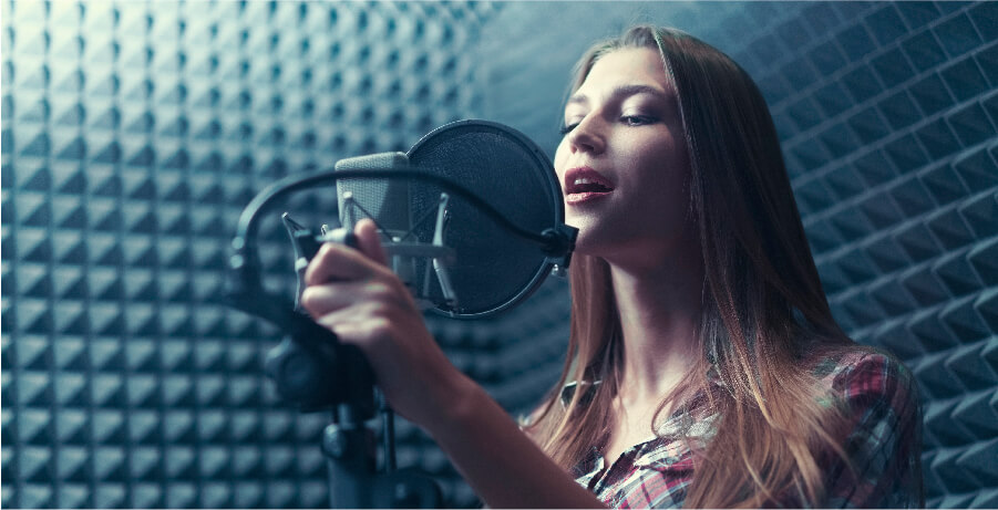 Mujer cantando frente a un micrófono profesional dentro de una cabina de grabación